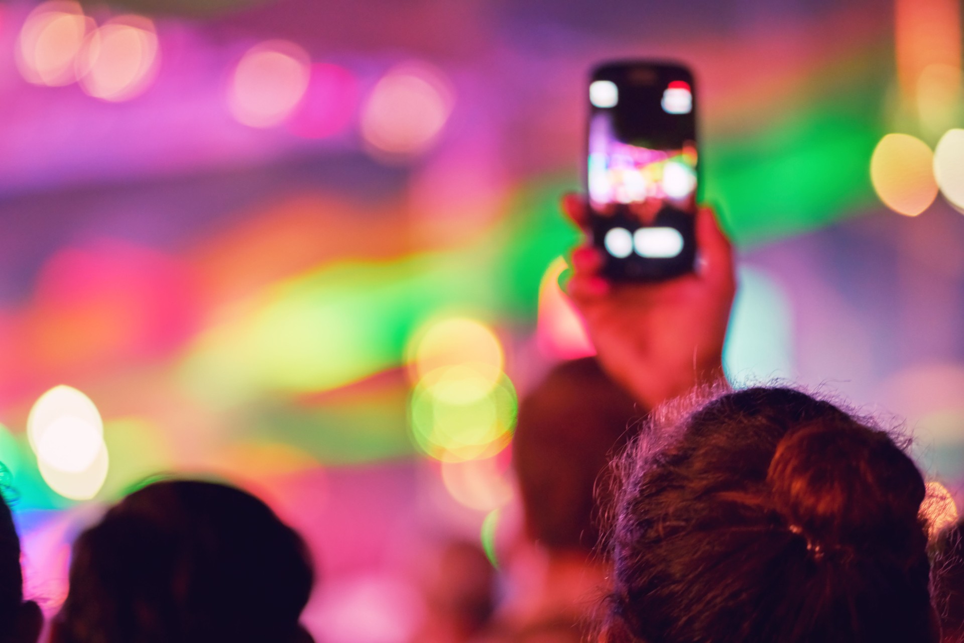 Verschwommene Silhouette eines Mädchens schießt ein Konzert auf einem Smartphone. Jugendmusikfestival der Popmusik. Lasershow auf der Bühne. Die Menge der Fans. Unverschwommene bokeh Grundhintergrund für Design